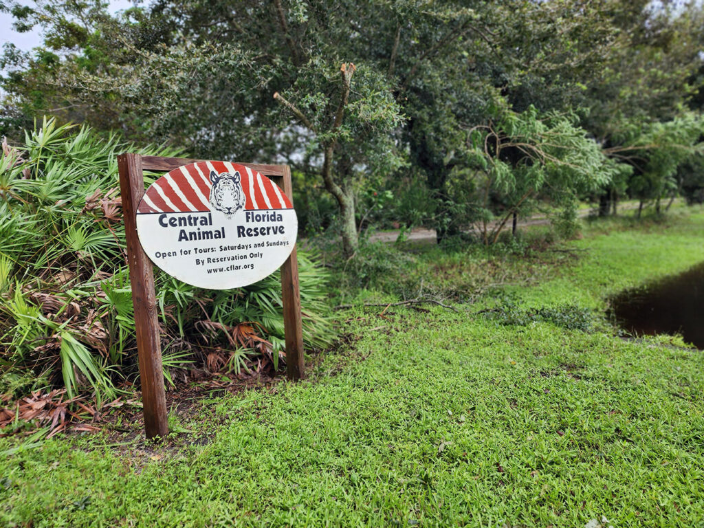 A sign for Central Florida Animal Reserve stands on grass near trees and a small pond, advertising tours on weekends and by reservation only.