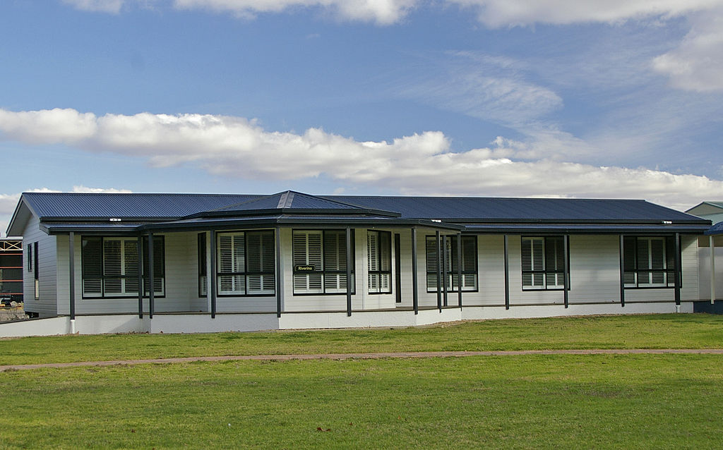 Single-story, modern prefabricated house with a dark roof, large windows, and a covered porch, set on a grassy lawn near Central Florida Animal Reserve under a partly cloudy sky.