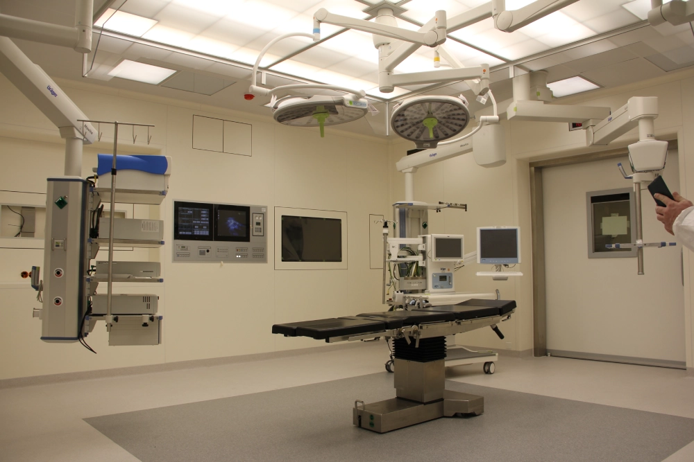 An empty, modern operating room with surgical lights, medical equipment, monitors, and an operating table under bright ceiling lights—reflecting the safety standards championed by the CFAR 3 V’s Campaign.