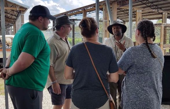 A group of five adults stands outdoors in conversation near a metal structure at Central Florida Animal Reserve, with one person gesturing while speaking.